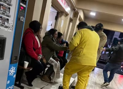 Bomberos voluntarios uniformados distribuyen alimentos calientes a personas sentadas en el interior del Hospital de Ñemby durante la noche, en el marco de su programa solidario de asistencia a vulnerables por las bajas temperaturas.