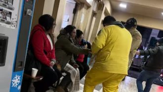 Bomberos voluntarios uniformados distribuyen alimentos calientes a personas sentadas en el interior del Hospital de Ñemby durante la noche, en el marco de su programa solidario de asistencia a vulnerables por las bajas temperaturas.