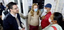 La ministra de Salud María Teresa Barán, vestida con campera beige y barbijo azul, conversa con personal médico y funcionarios durante su visita de inspección al Hospital General de Lambaré. En la imagen se observa al viceministro Saúl Recalde con anteojos y saco azul marino, junto a profesionales de la salud con uniformes y barbijos en los pasillos del centro hospitalario.