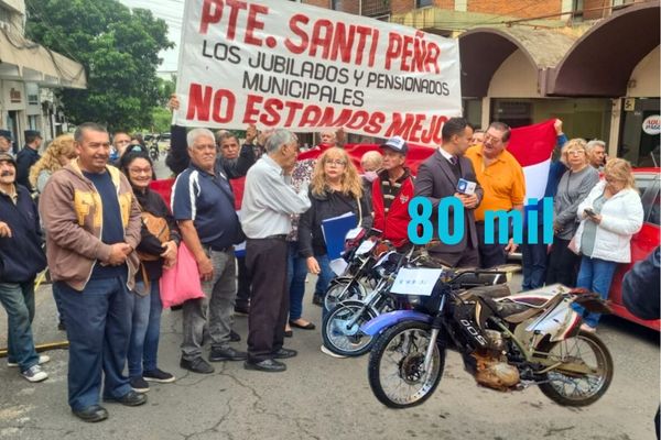 Grupo de jubilados y pensionados municipales manifestándose con pancartas que dicen "PTE. SANTIAGO PEÑA LOS JUBILADOS Y PENSIONADOS MUNICIPALES NO ESTAMOS MEJOR" frente a una motocicleta con el precio "G. 80 mil" superpuesto, en protesta por la venta patrimonial de la Caja Municipal mientras esperan el pago de sus jubilaciones.